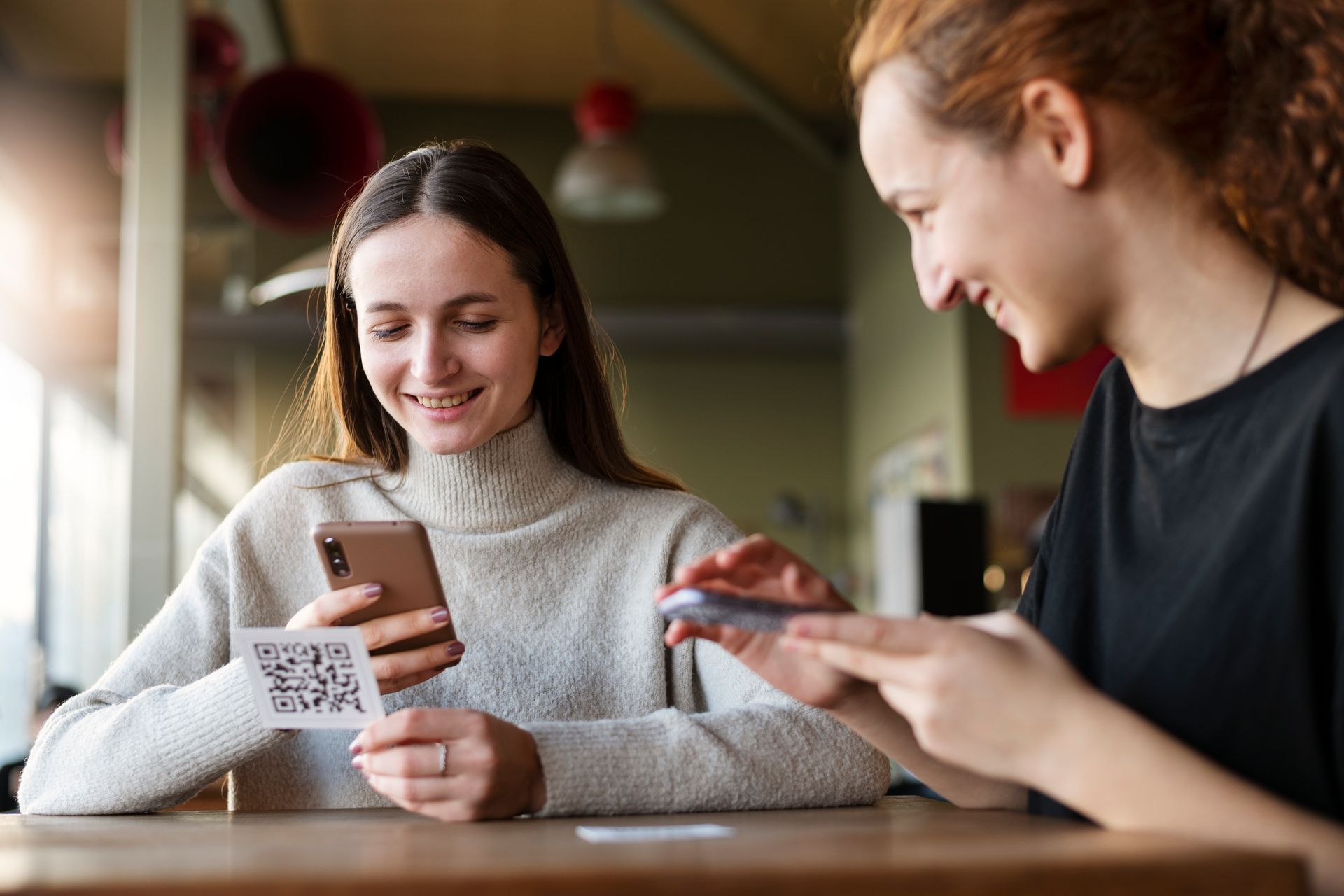 Two ladies with mobile phones smiling while one scans a QR code with her phone