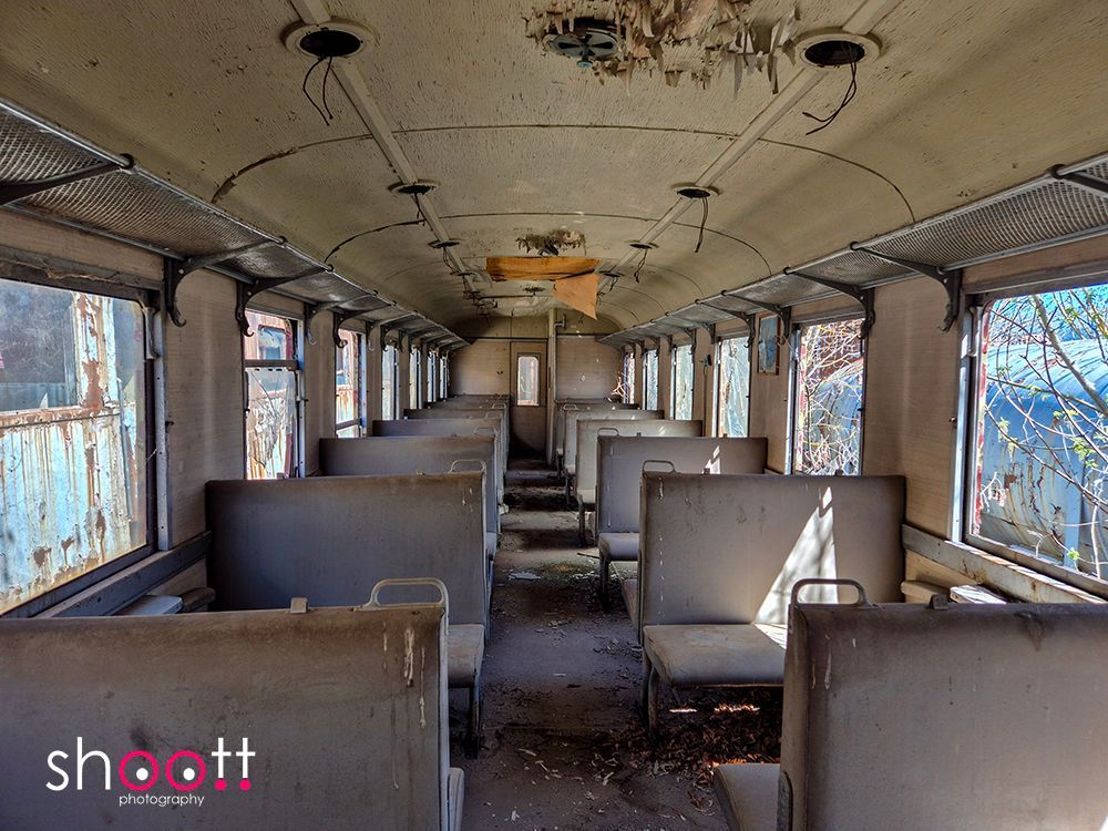 Het interieur van een verlaten, vervallen treinstel met stoffige, versleten stoelen en blootliggende bedrading die van het plafond hangt.