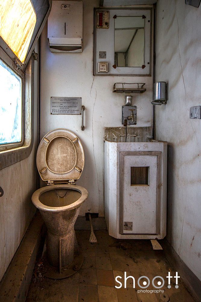 Een afgeleefde, kleine badkamer met een toilet en een wastafel in een vervallen treinstel.