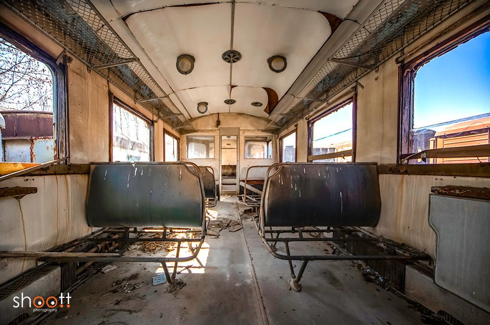 Het interieur van een vervallen, verlaten treinstel met donkere stoelen, verweerde muren en kapotte plafondpanelen.