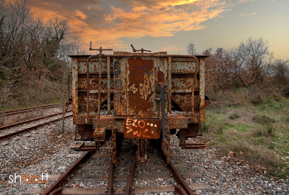 Een verroeste, verweerde treinwagon staat op de rails tegen een zonsondergang.