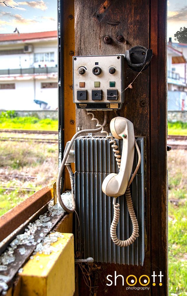 Een oude, aan de muur gemonteerde telefoon met bedieningspaneel in een vervallen treinstel, met gebroken glas op de vensterbank.