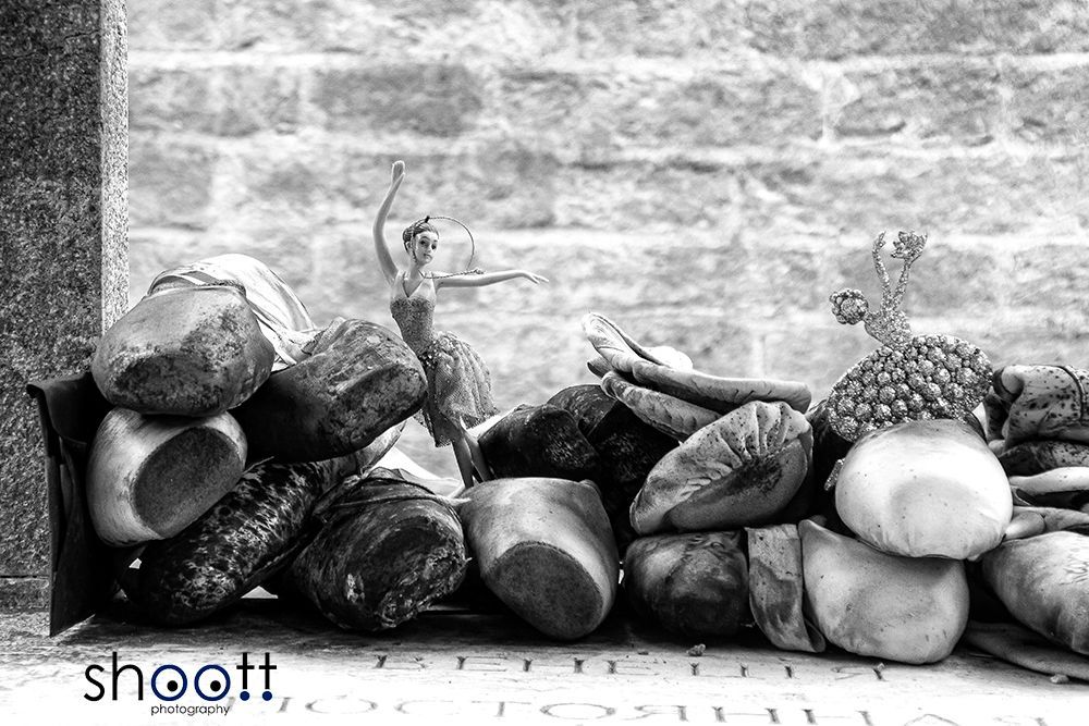 Een klein ballerinaatje danst te midden van een stapel balletschoenen tegen een bakstenen achtergrond van het graf van een beroemde choreograaf.