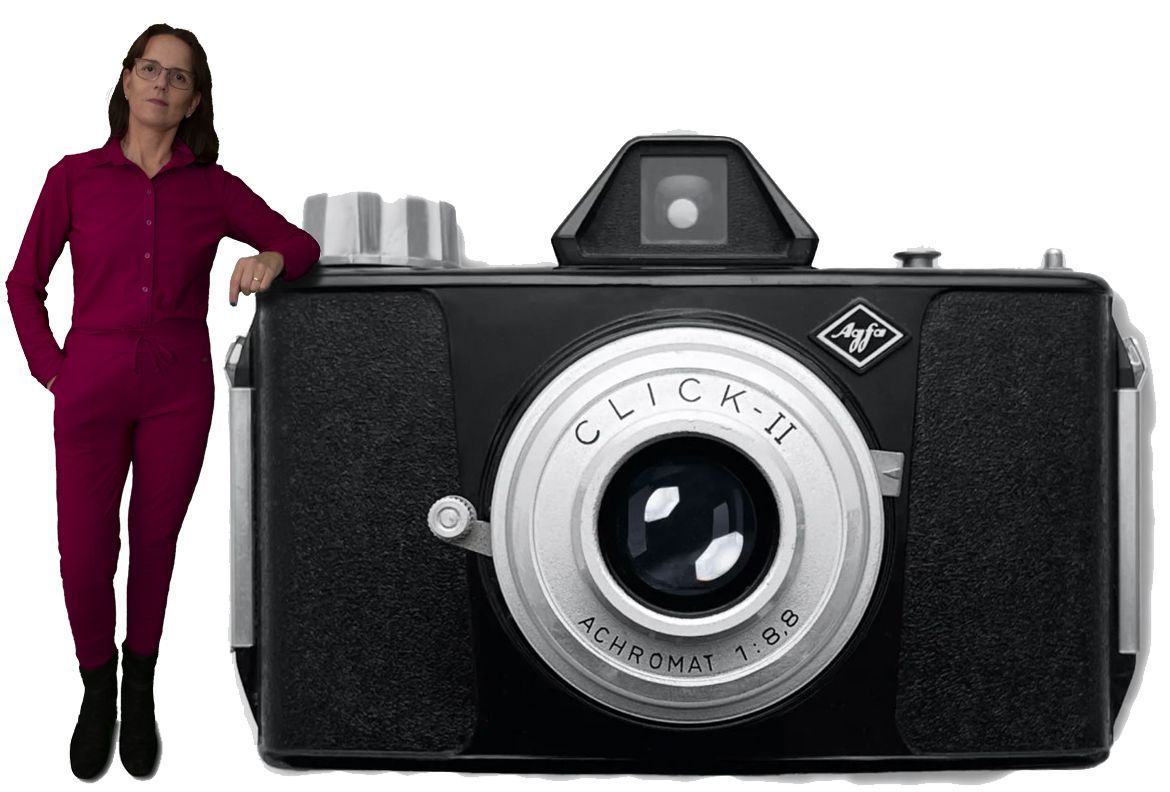 Een persoon in een magenta overall staat naast een extra grote Agfa Click-II camera.