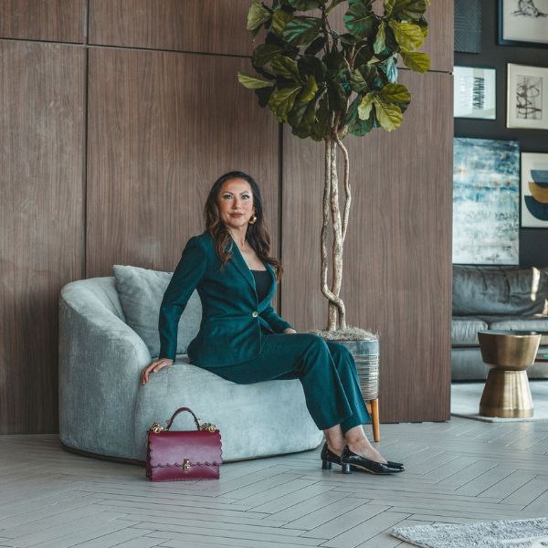 A woman in a suit is sitting on a chair in a living room.