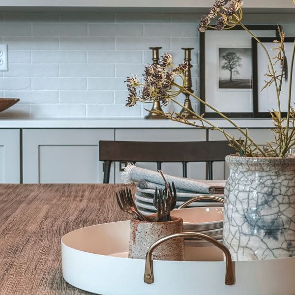A tray with a vase of flowers on it sits on a wooden table.