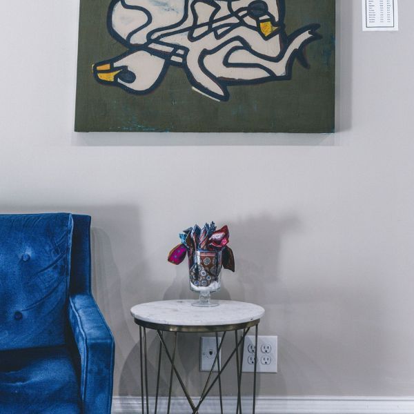 A living room with a blue chair a table and a painting on the wall