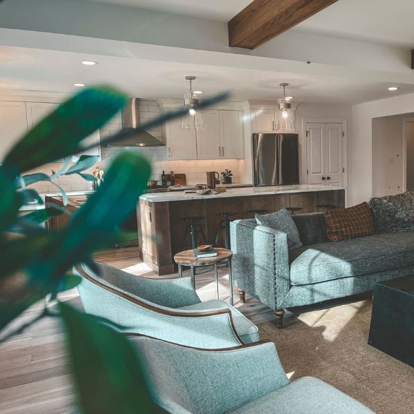 A living room with a couch and chairs and a kitchen in the background.