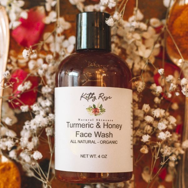 A bottle of turmeric and honey face wash is surrounded by flowers