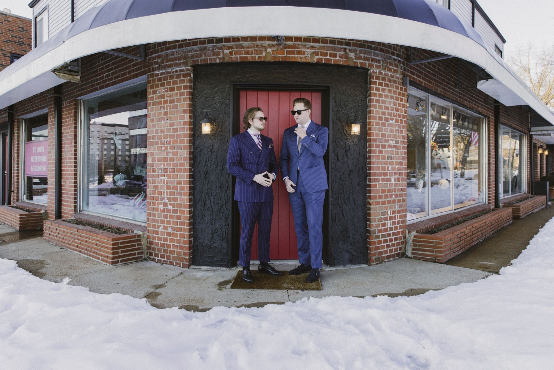 Two men in suits are standing in front of a red door.