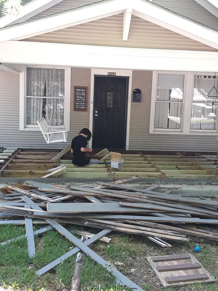 A man is sitting on a pile of wood in front of a house.