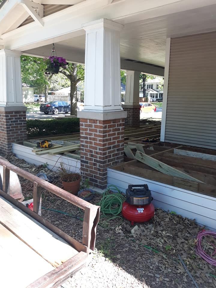 A red air compressor is sitting in front of a house under construction.