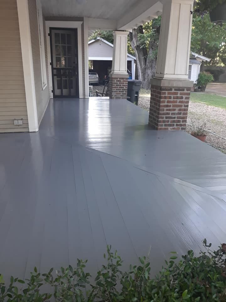 The porch of a house is painted gray and has a brick pillar.