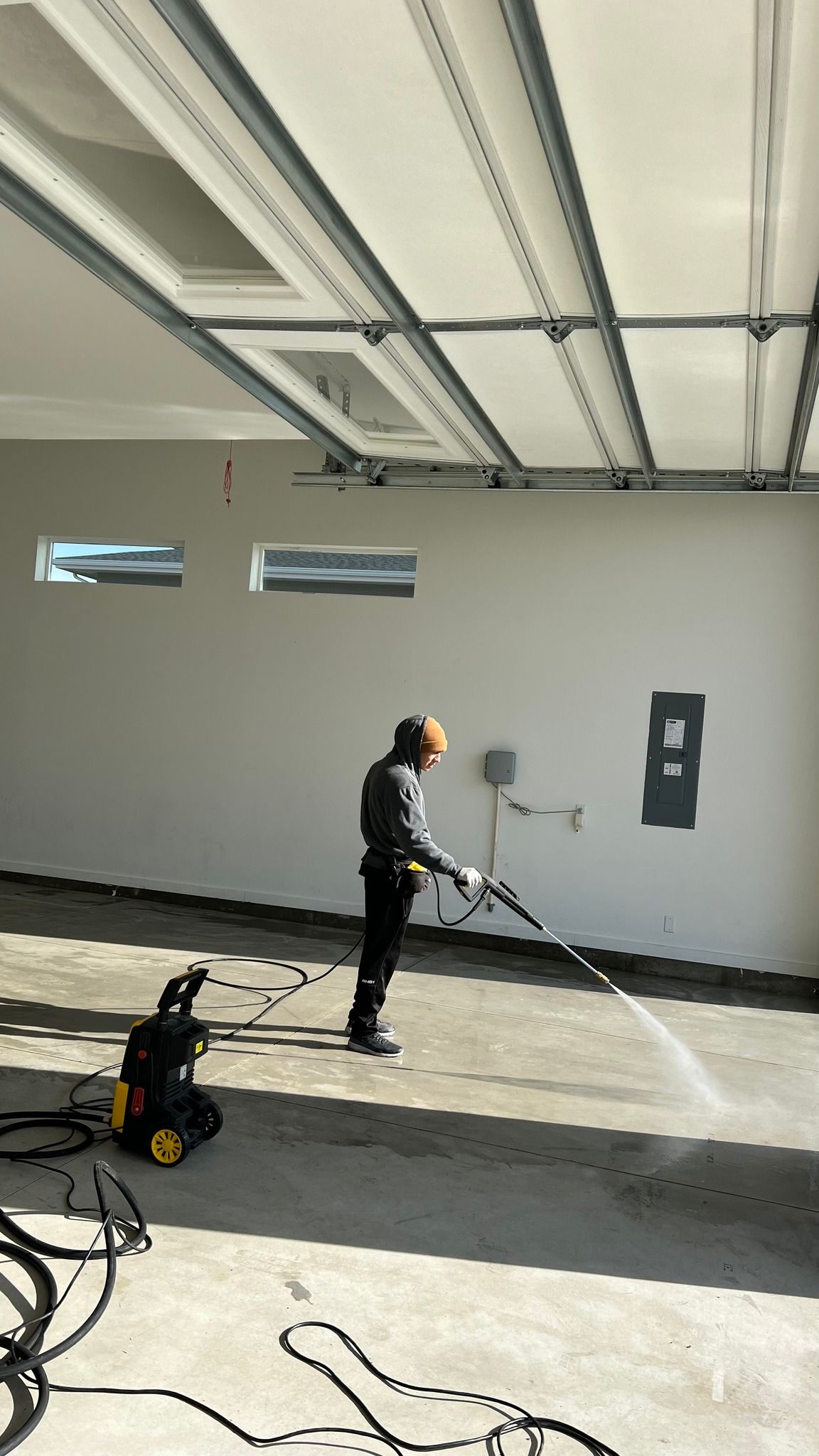 A man is using a high pressure washer to clean a garage floor.