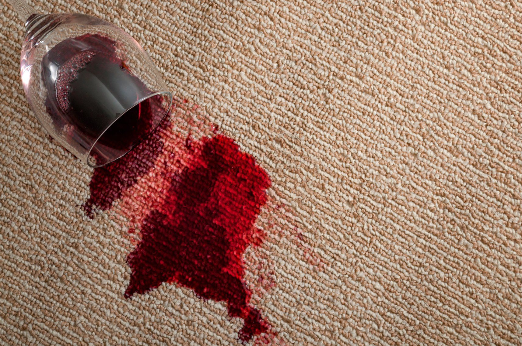 Spilled red wine from a tipped glass on beige fabric