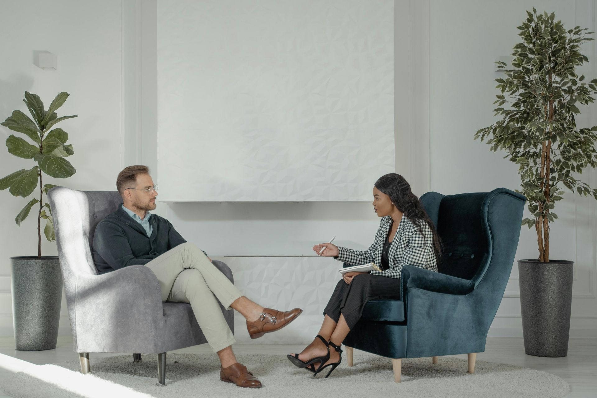 A man and a woman are sitting in chairs talking to each other.
