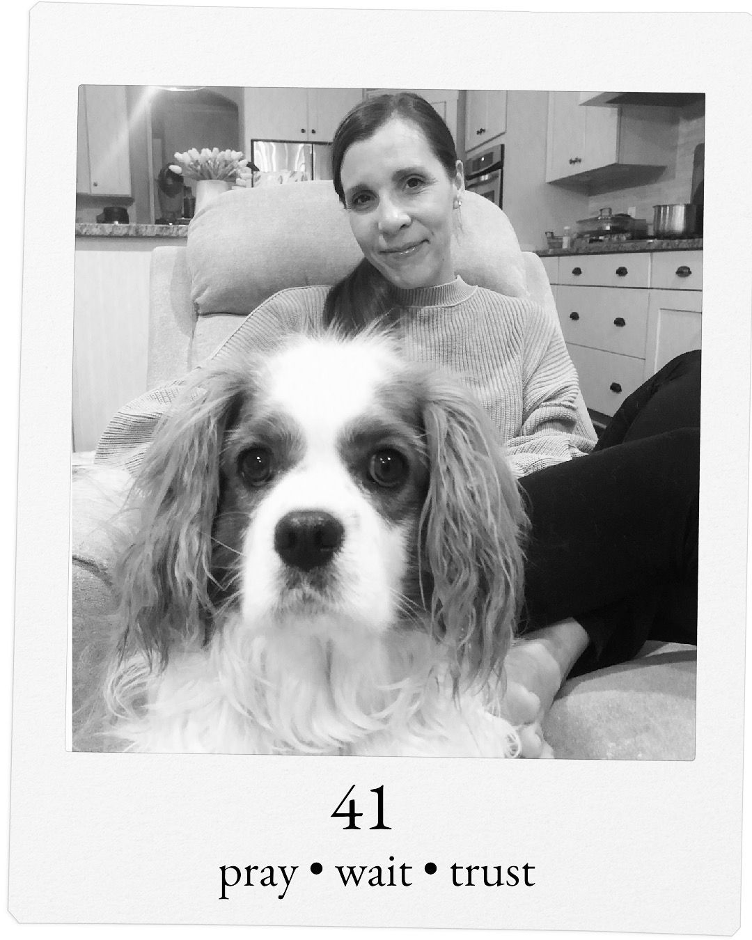 Black and white of Amy smiling in recliner with her dog at her feet front and center in phot