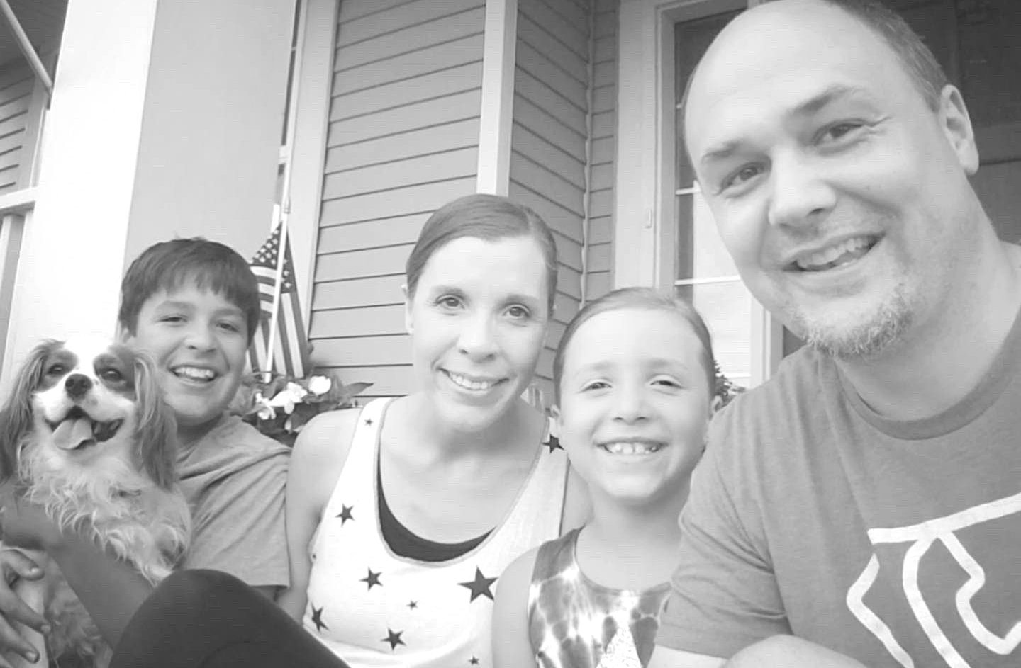 Amy and all of family including dog sitting on the porch in Fourth of July outfits. Black and white.