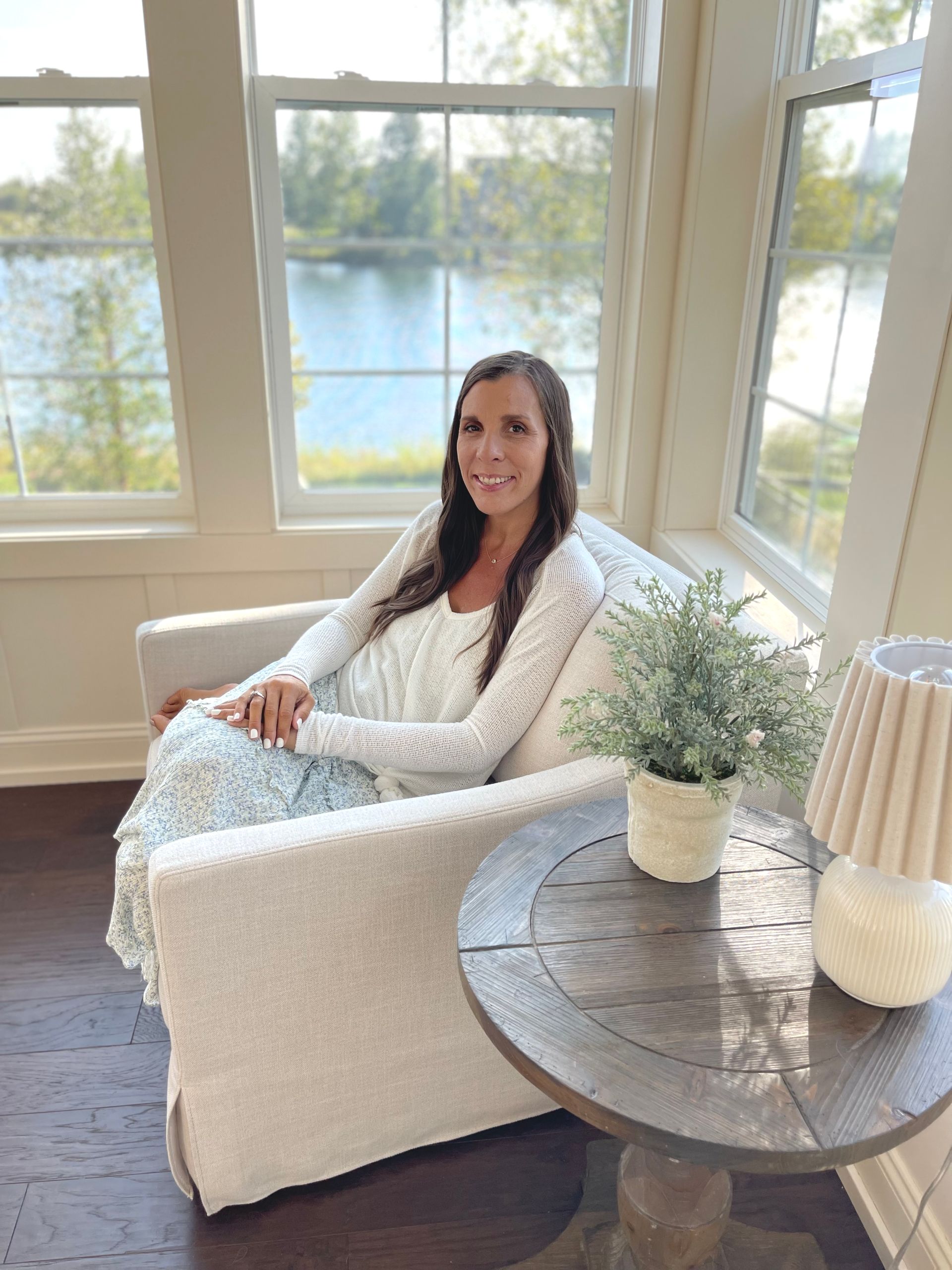 Amy sitting in chair smiling hair down and wavy curls ugg creamy slippers cream sweatshirt and jeans with holes.