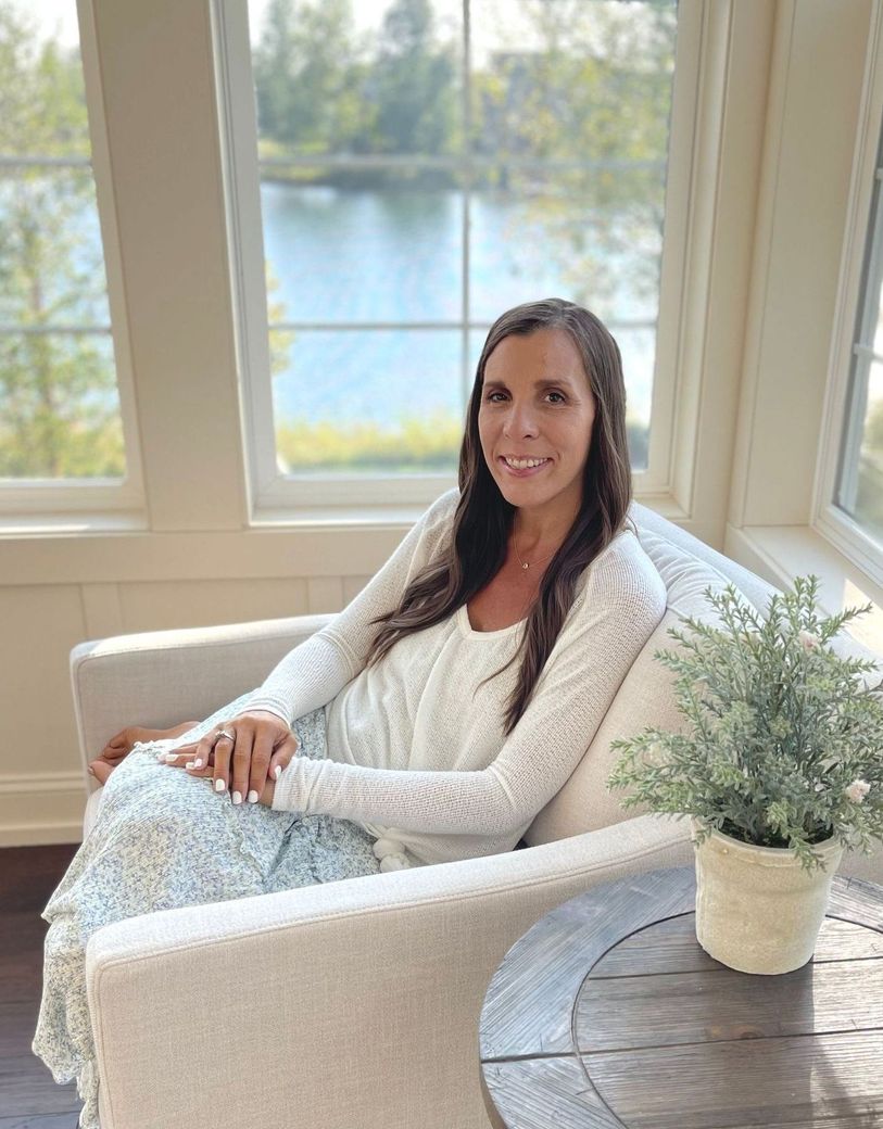 Amy sitting in chair smiling hair down and wavy curls ugg creamy slippers cream sweatshirt and jeans with holes.