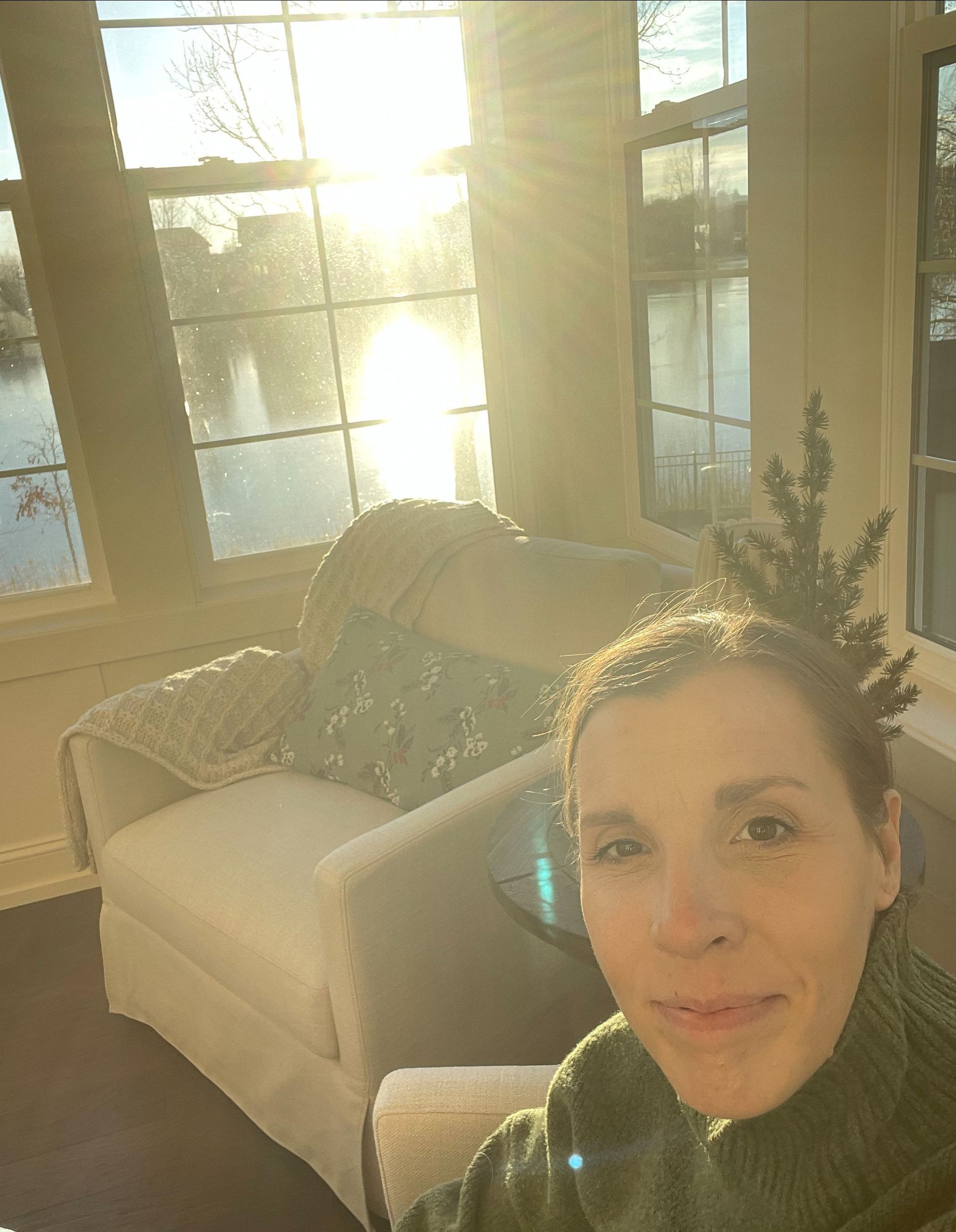 Amy in the sunroom with yellow sunlight streaming through the widows - entire photo is sunbathed yellow.  She has a half smile while taking a selfie.