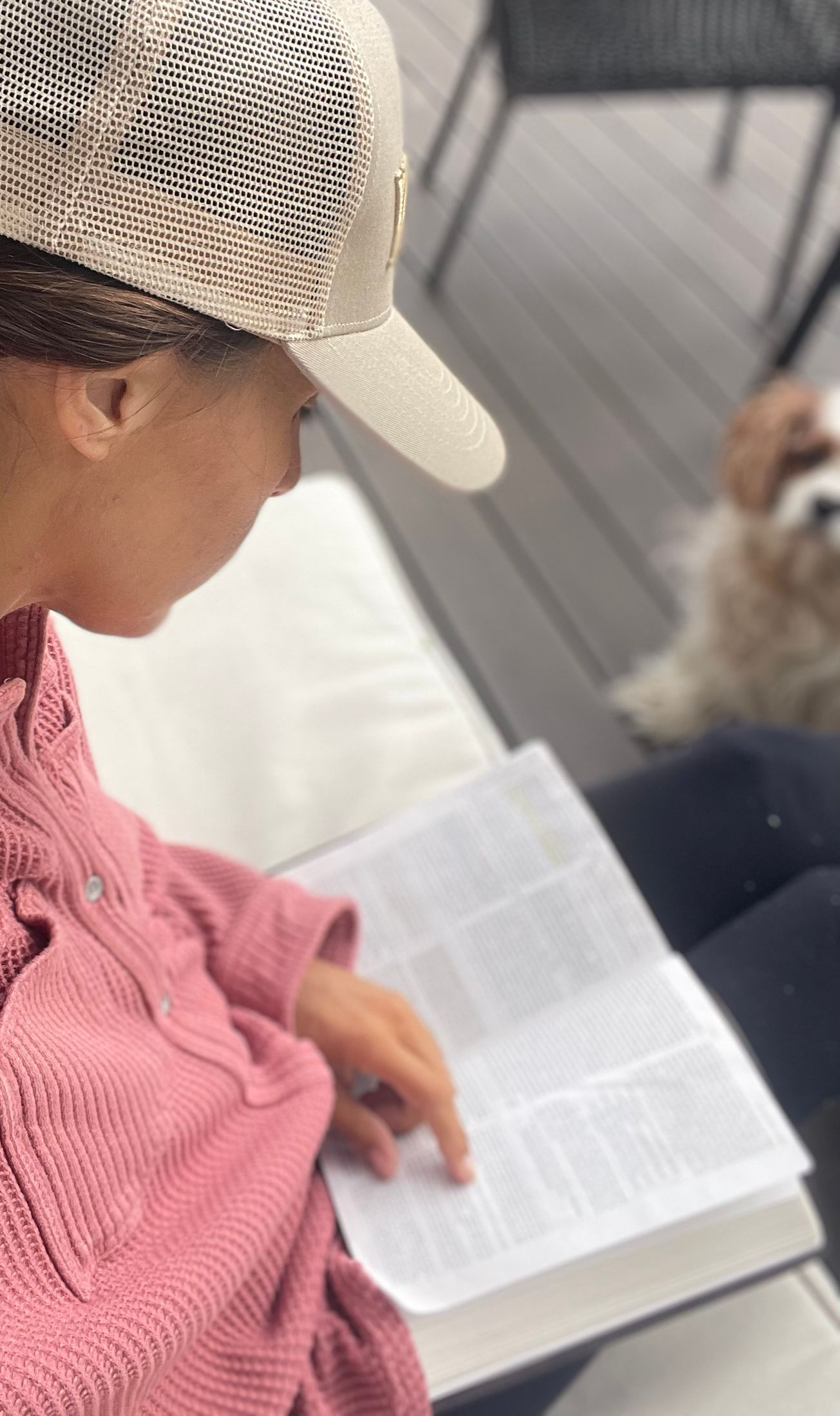 Amy from a side angle sitting on the porch with a hat, bible open on her lap with hand on the bible.