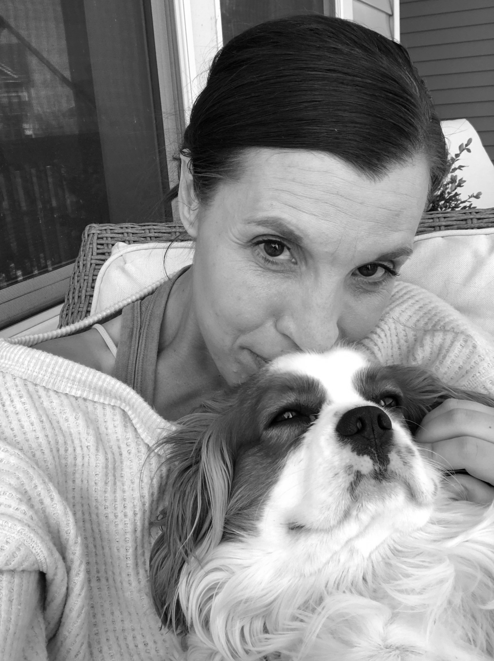 Black and white photo of Amy and Dog on proch sitting. Amy kissing  top of Cooper's head with happy look.