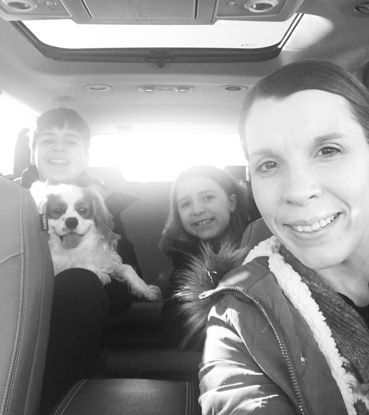 Amy and kids with dog in SUV. Black and White photo. All are smiling even the dog. Selfie style.