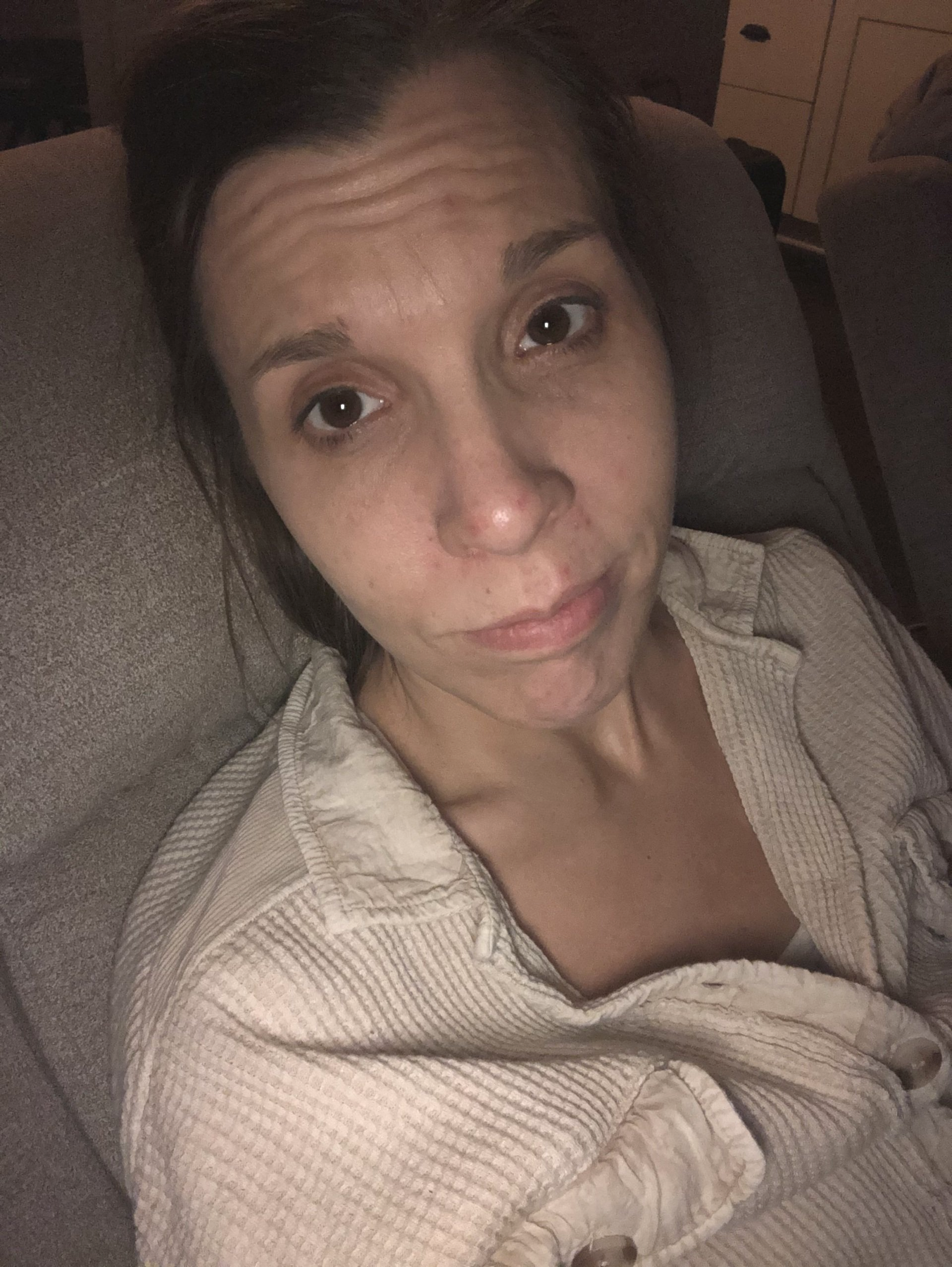 Amy laying back in recliner looking like she doesn't feel well in cream button up shirt