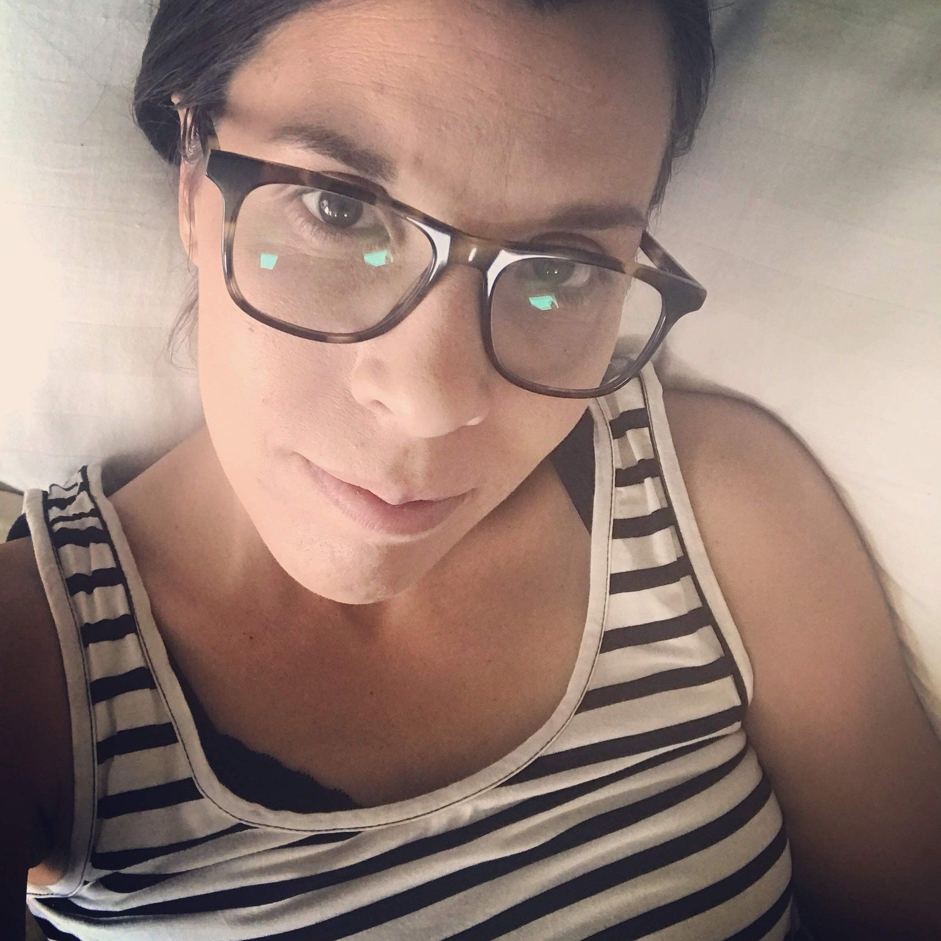 amy with black and white striped tank top and  glasses on.  Laying in bed with selfie photo.