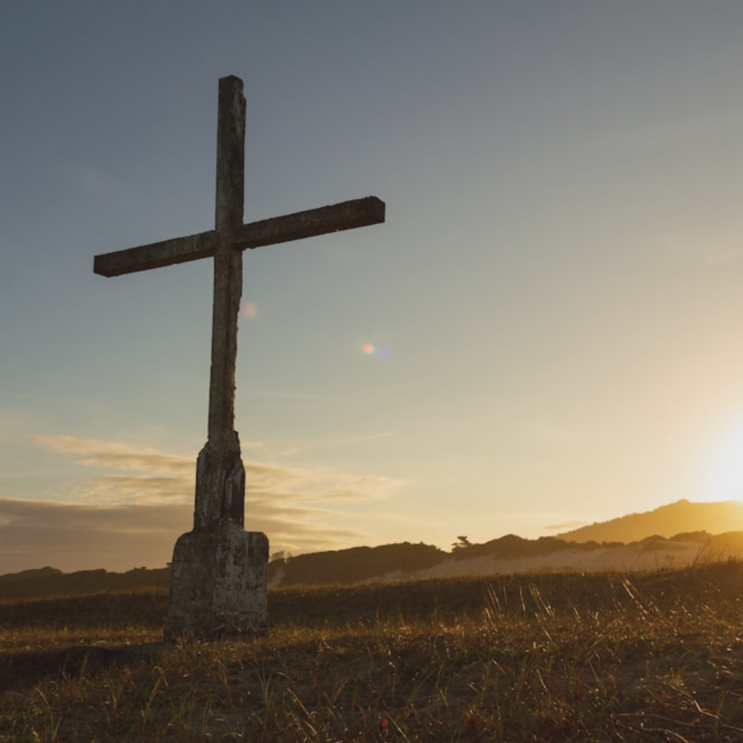 Photo of a cross on a hill with the sun setting.