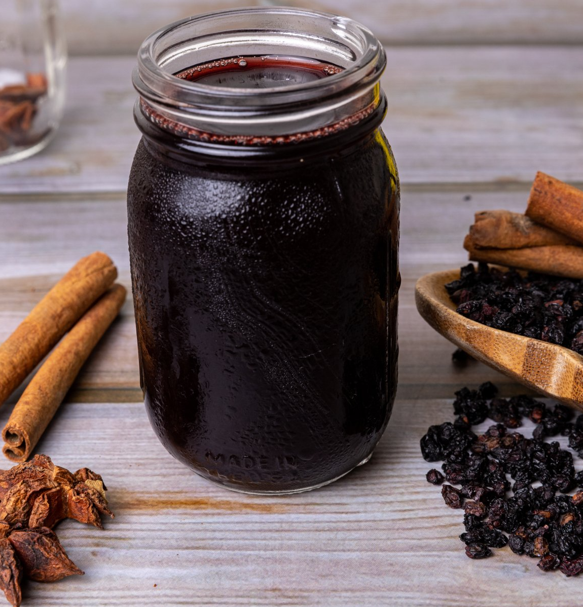 frosty mason jar with homemade elderberry syrup filled to the top dried elderberries and cinnamon