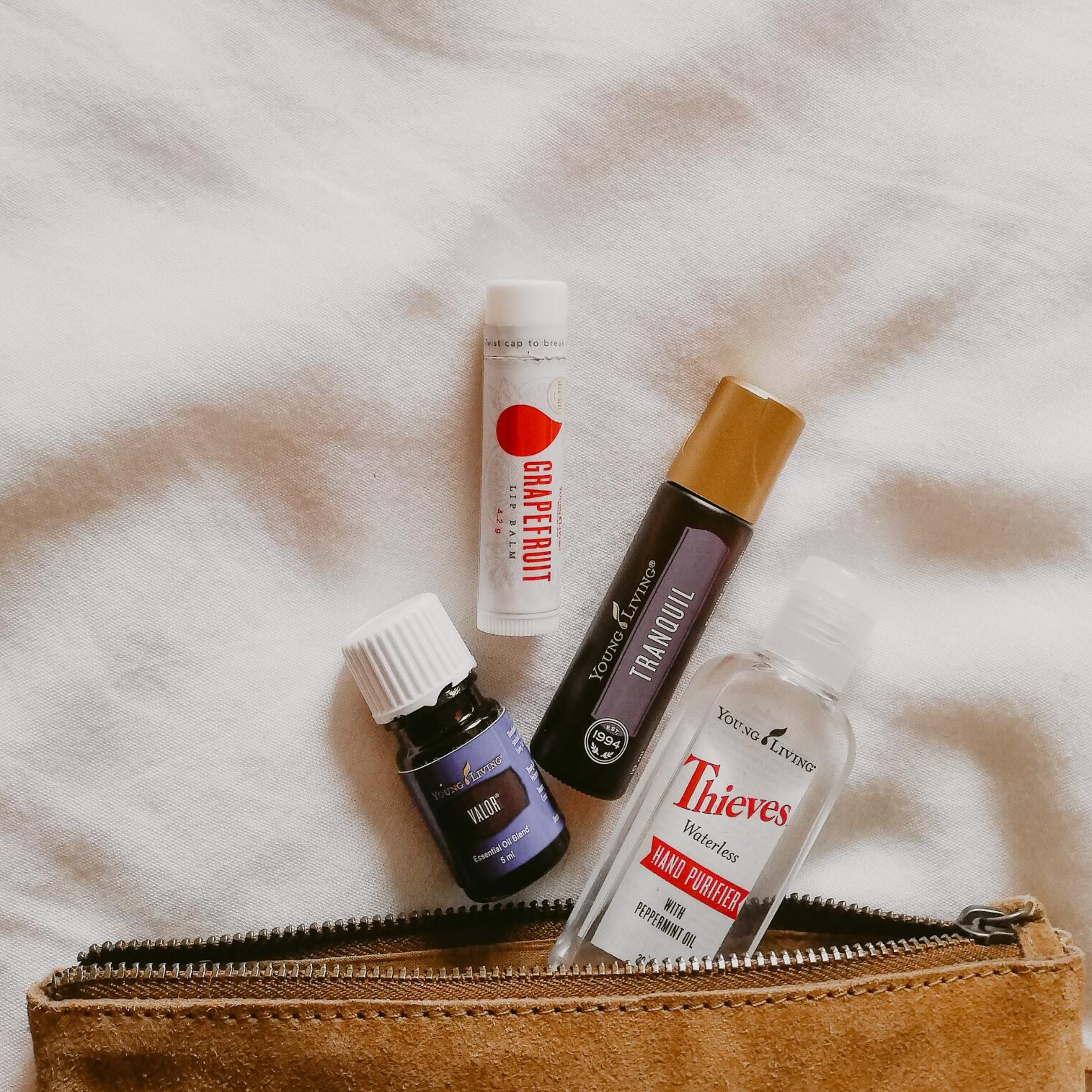 leather pouch spilling out with young living produts, including hand sanitizer lip gloss and 2 oilsl