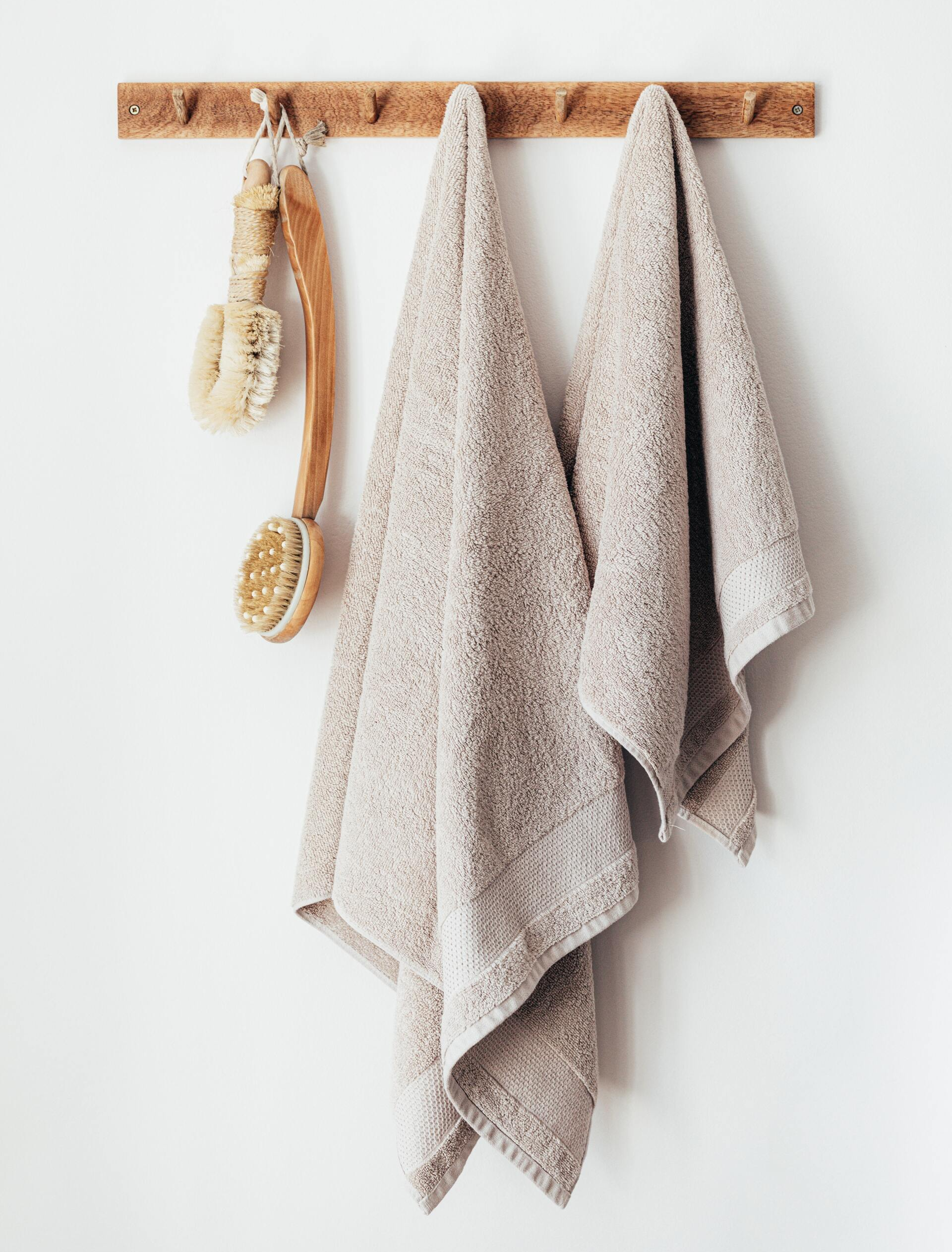 2 beige towels hanging on hooks with 2 dry brushes hanging next to them