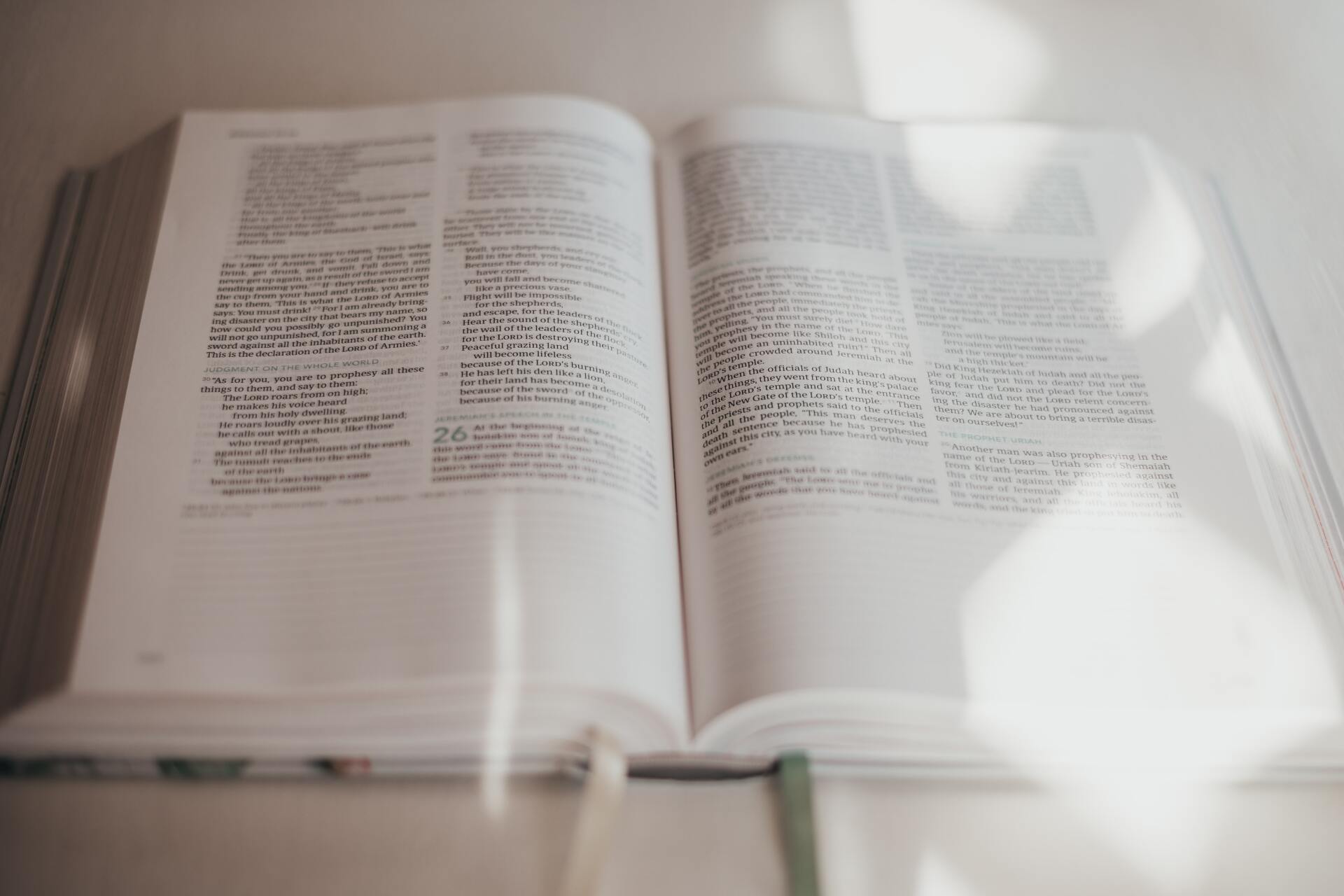 open bible with attached string bookmark hanging on sitting on table and  sun shadows over it