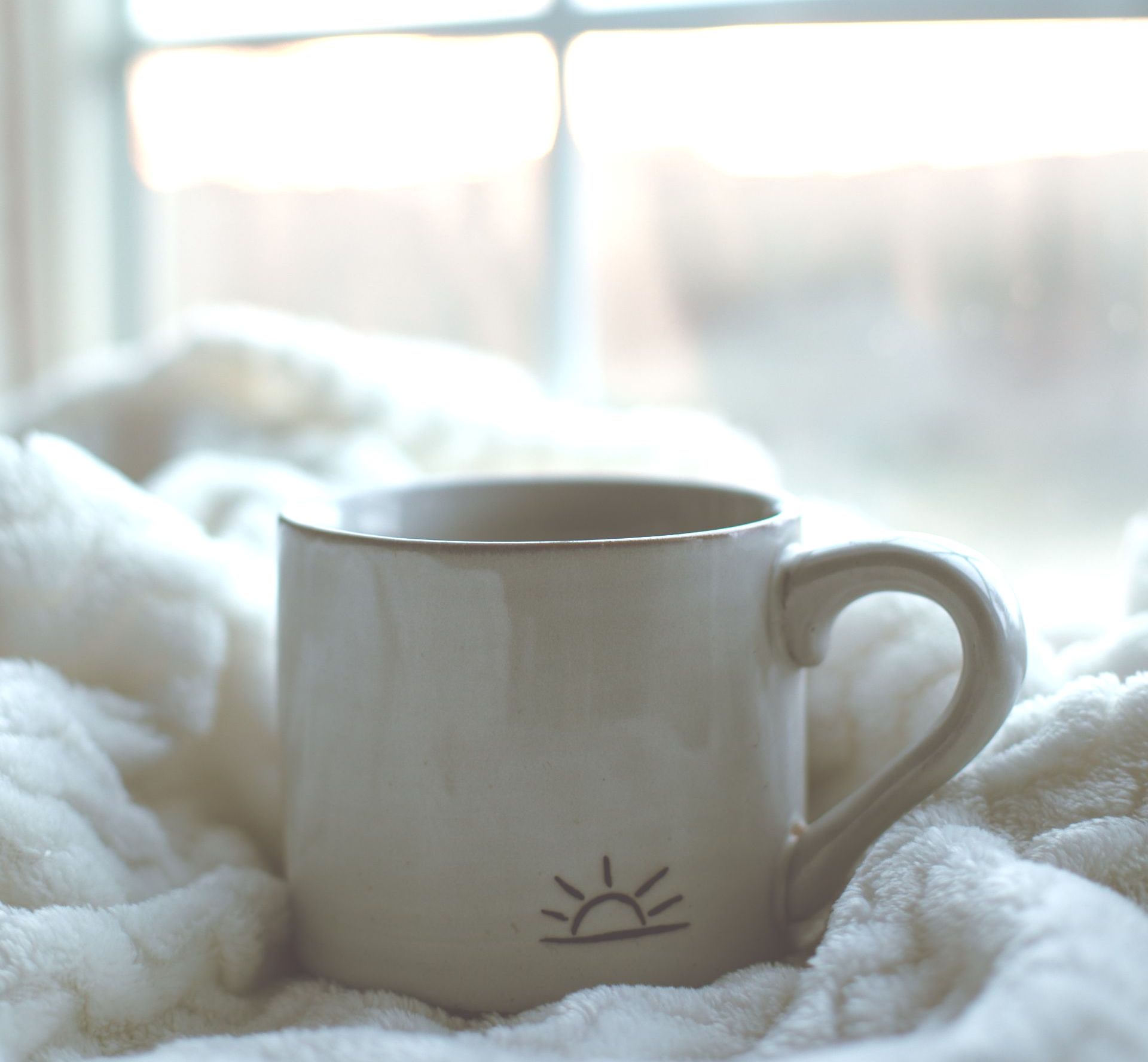 coffee mug with image of sunrise on cozy blanket. Faded window in the background.