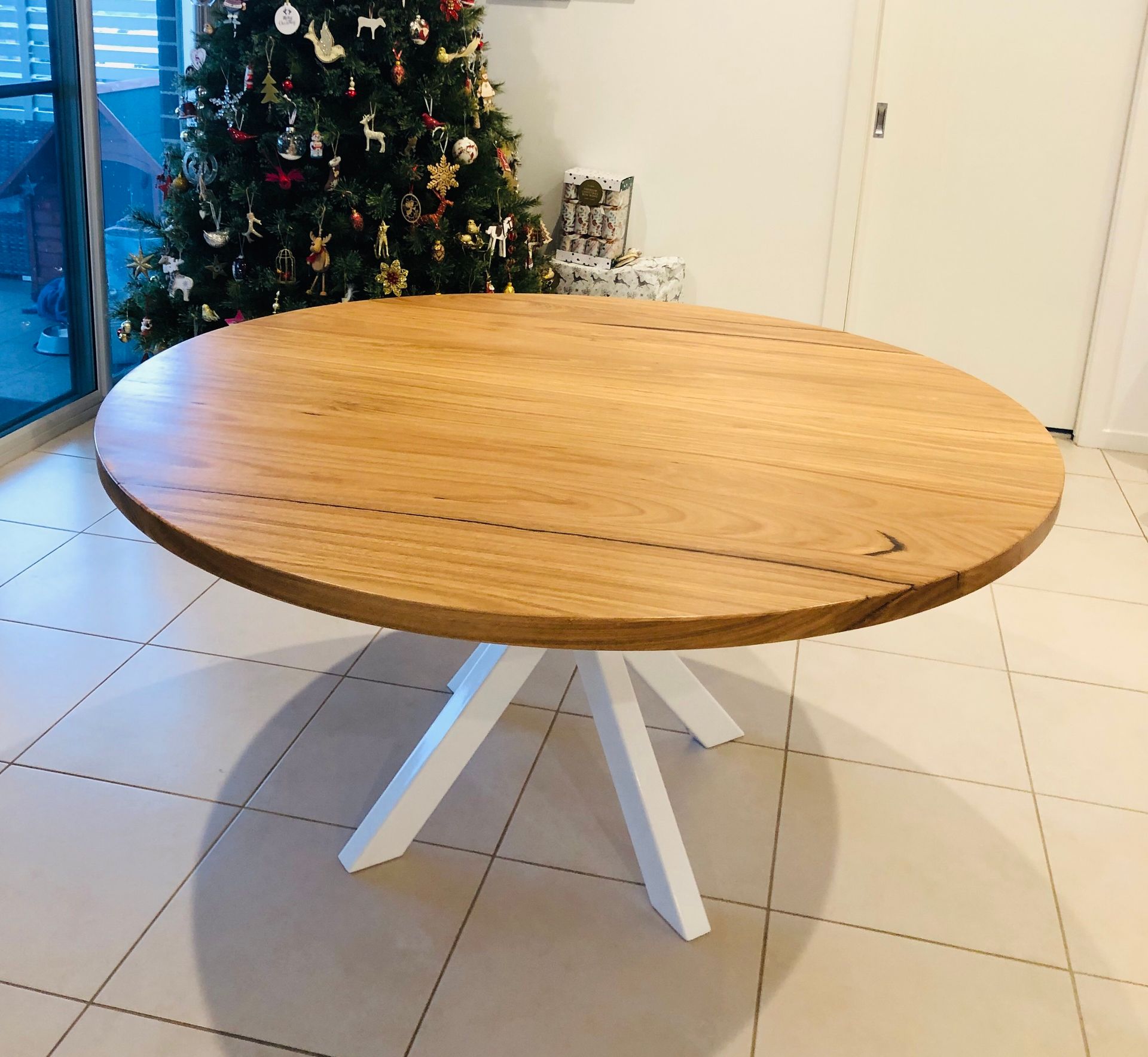 A round wooden table with white legs on tiles — Marlix Custom Timber Furniture Design and Joinery in Unanderra, NSW