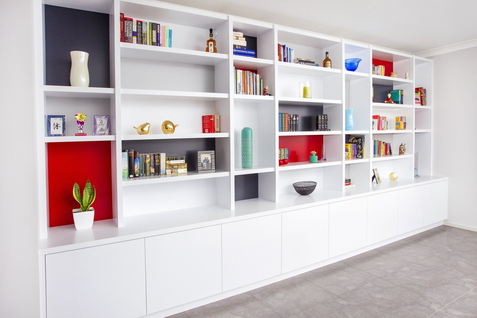 A Room with A Long Wall of Shelves Filled with Books and Decorations — Marlix Custom Timber Furniture Design and Joinery in Unanderra, NSW