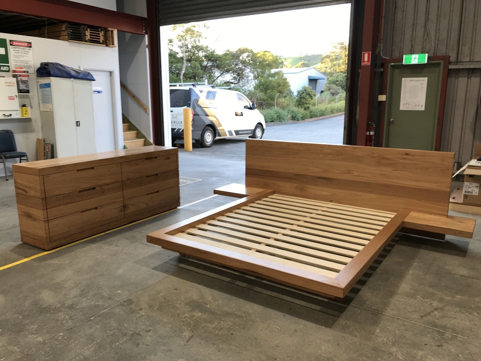 A Wooden Bed Is Sitting In A Warehouse Next To A Dresser — Marlix Custom Timber Furniture Design and Joinery in Unanderra, NSW
