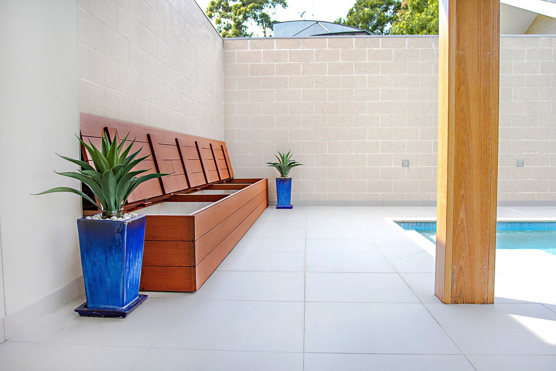 A Patio With A Bench And Two Potted Plants Next To A Swimming Pool — Marlix Custom Timber Furniture Design and Joinery in Unanderra, NSW
