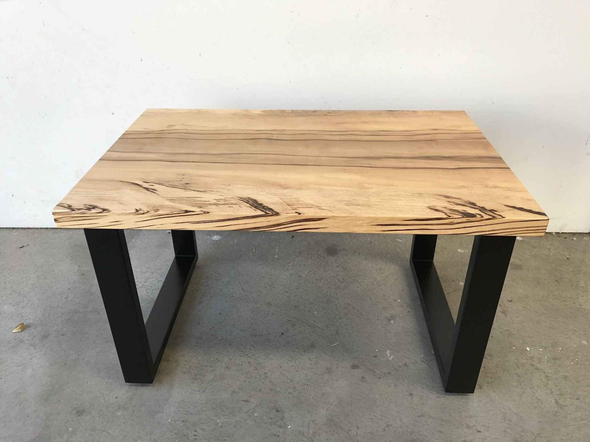 A Wooden Table With Black Legs Is Sitting On A Concrete Floor — Marlix Custom Timber Furniture Design and Joinery in Unanderra, NSW