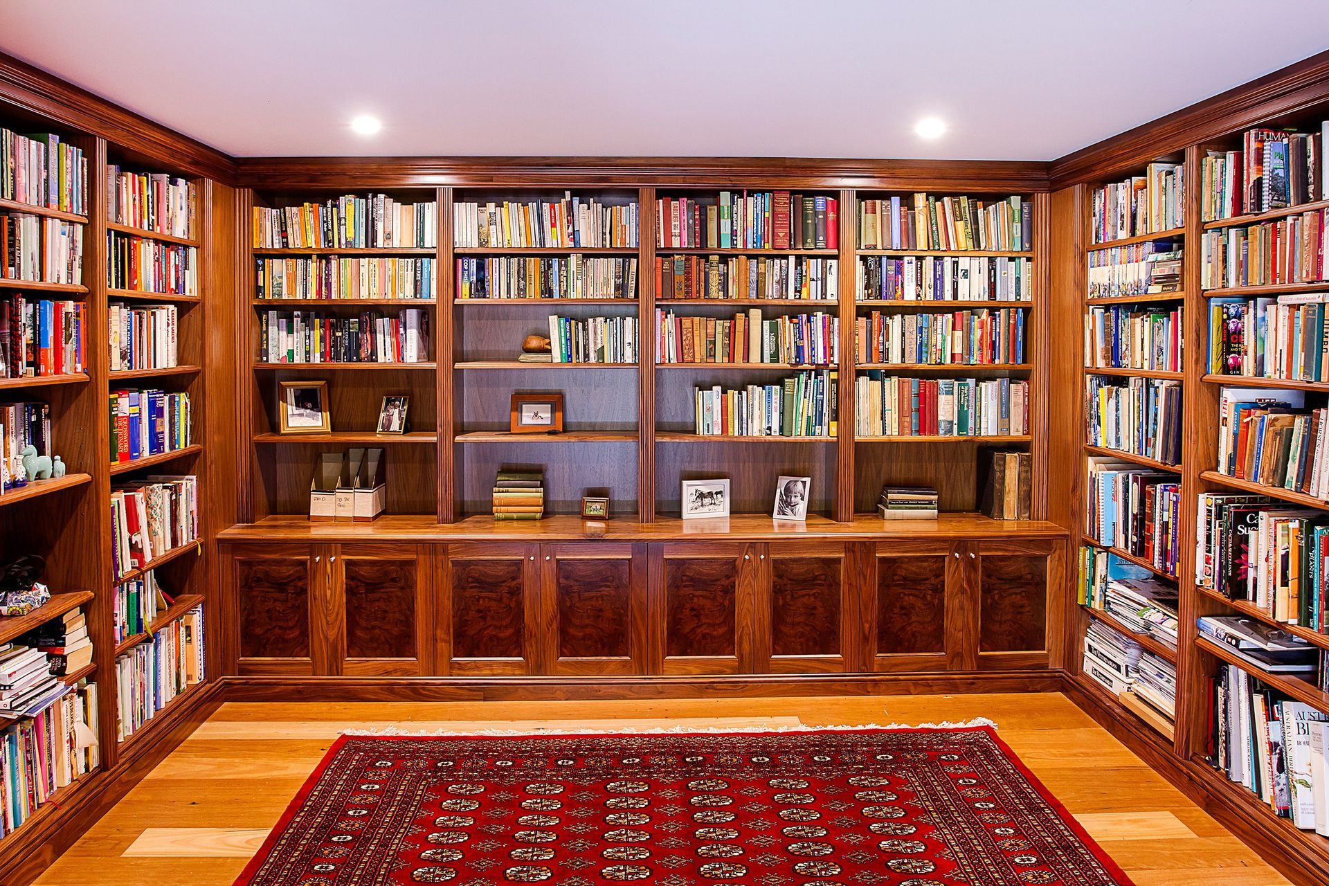 A large wooden bookcase with lots of books and a red carpet on the floor — Marlix Custom Timber Furniture Design and Joinery in Unanderra, NSW