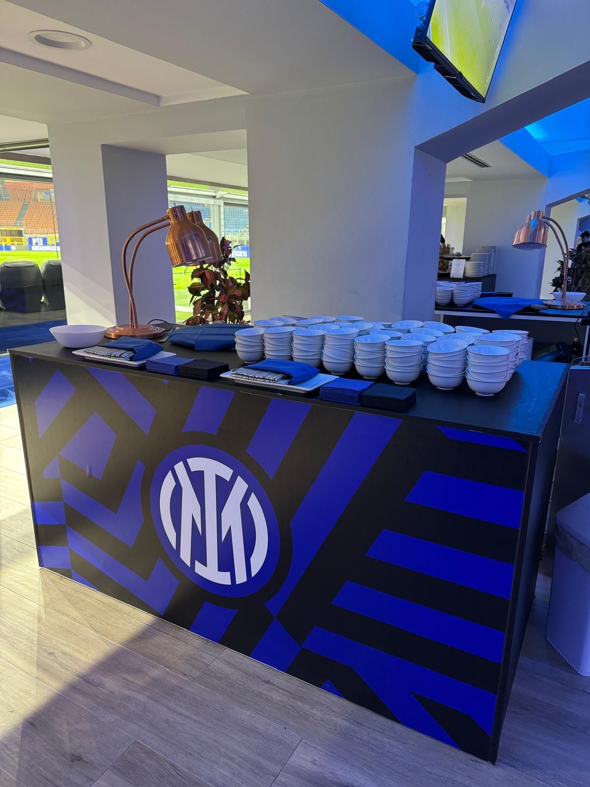 Un tavolo con il logo dell'Inter, con tazze, snack e vista sullo stadio.