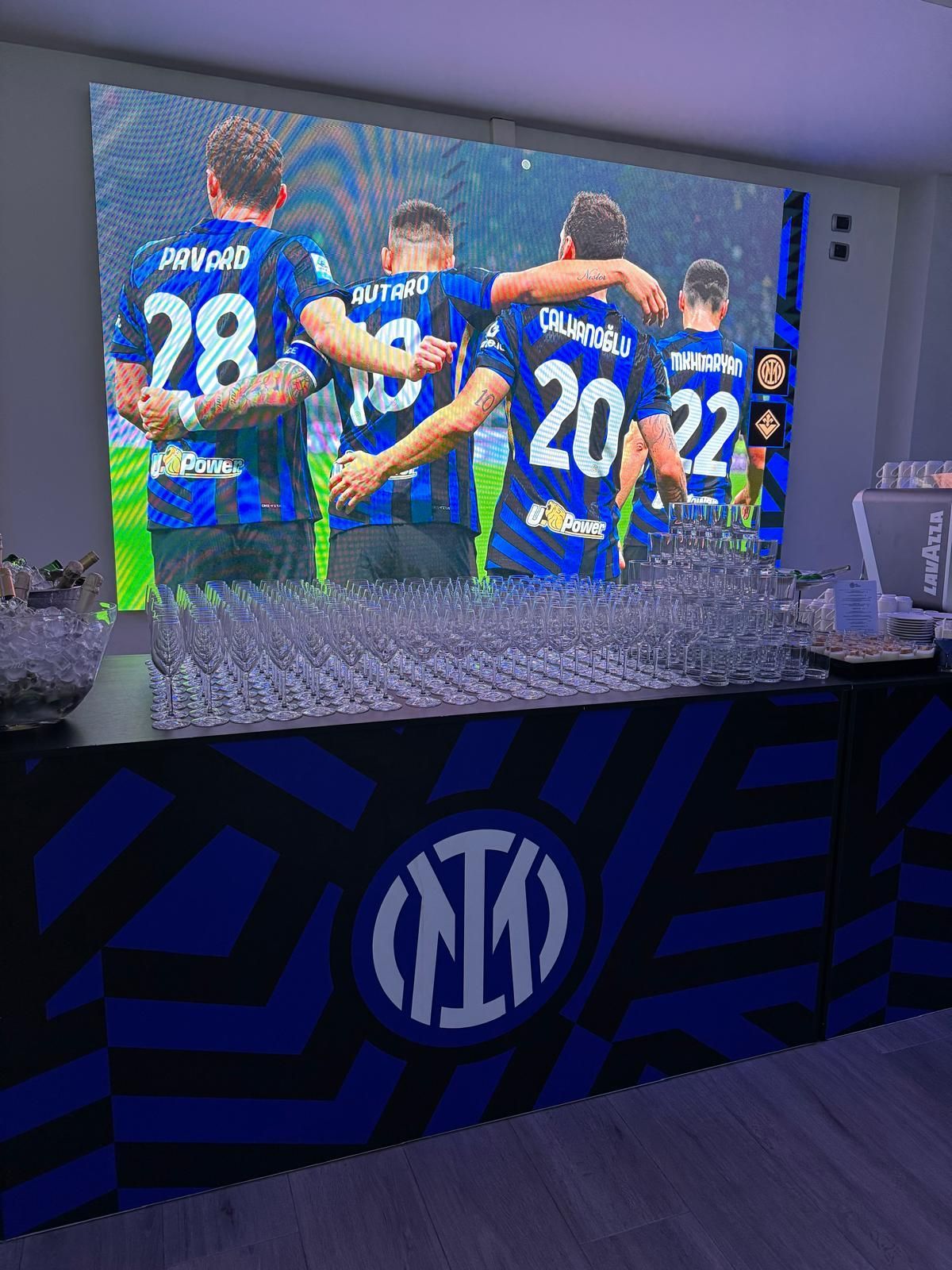 Bar con il logo dell'Inter, TV che mostra i giocatori di calcio in divisa blu che festeggiano.