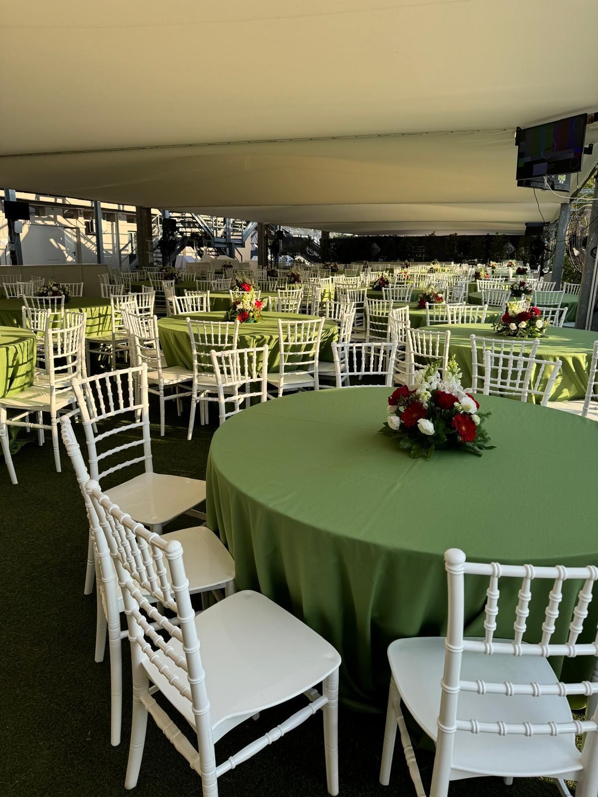 Spazio per eventi con tavoli rotondi ricoperti di tovaglie verdi, sedie bianche e centrotavola floreali.