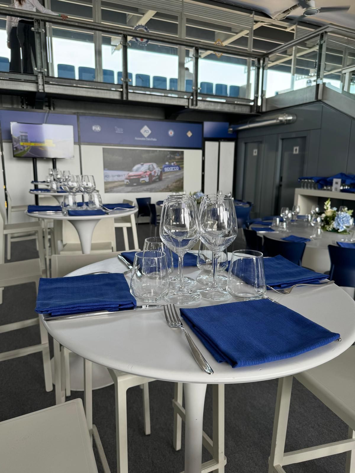 Eleganti tavoli da pranzo con tovaglioli blu apparecchiati in una suite da stadio, pronti per il pasto.