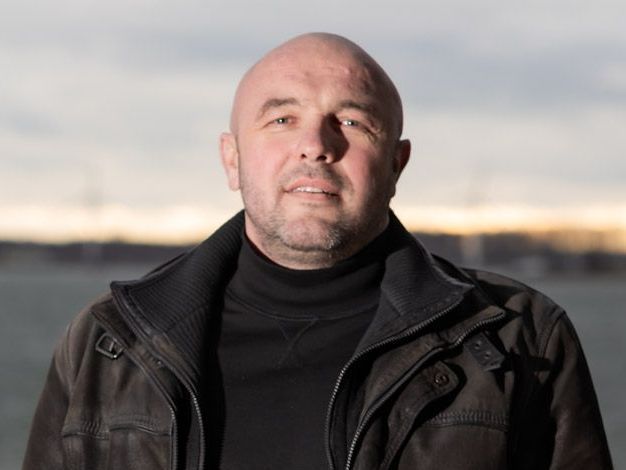 Een man met een blauwe helm en een geel vest buigt zijn arm.