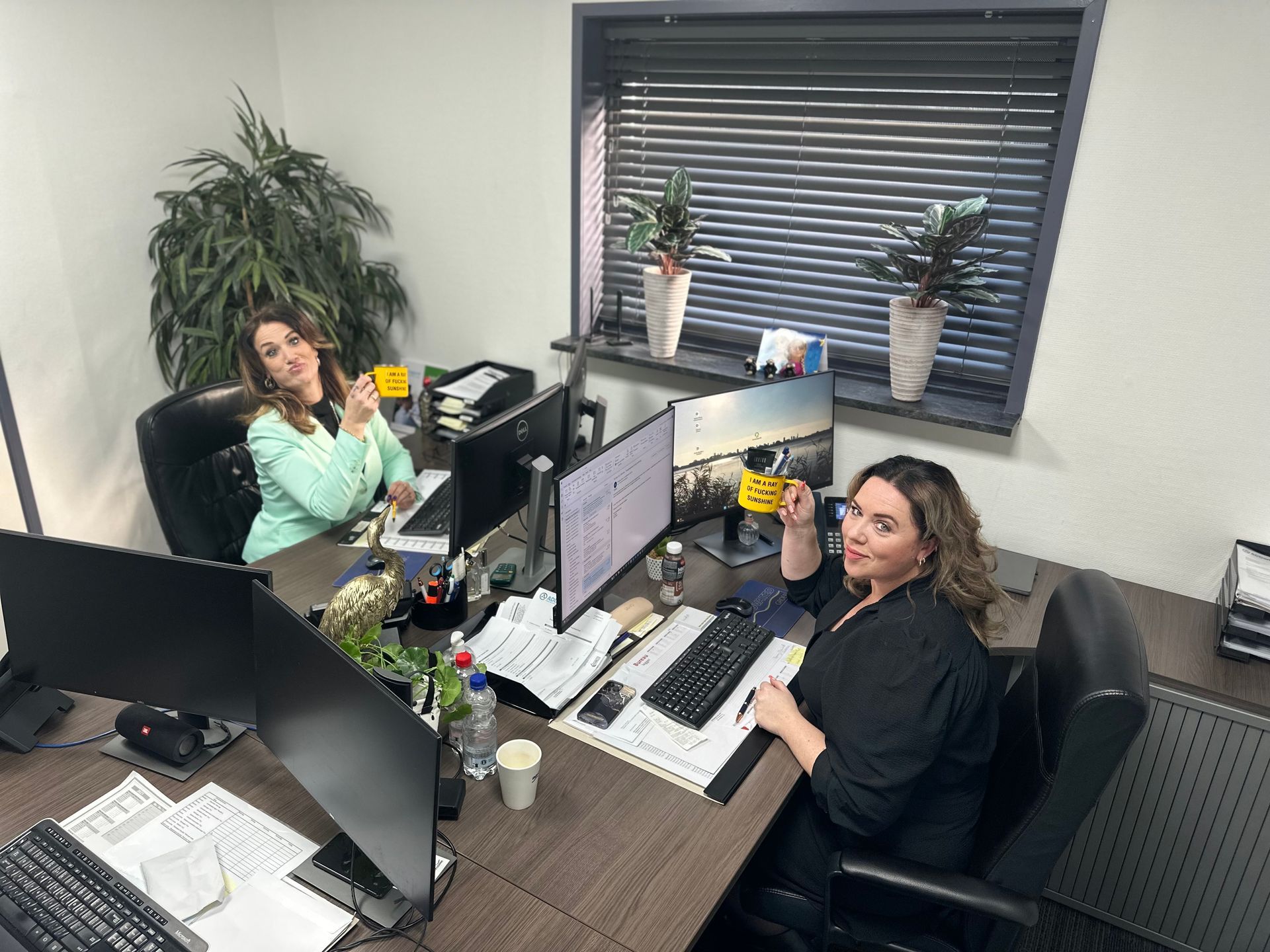 Twee vrouwen zitten aan een bureau in een kantoor met computers.