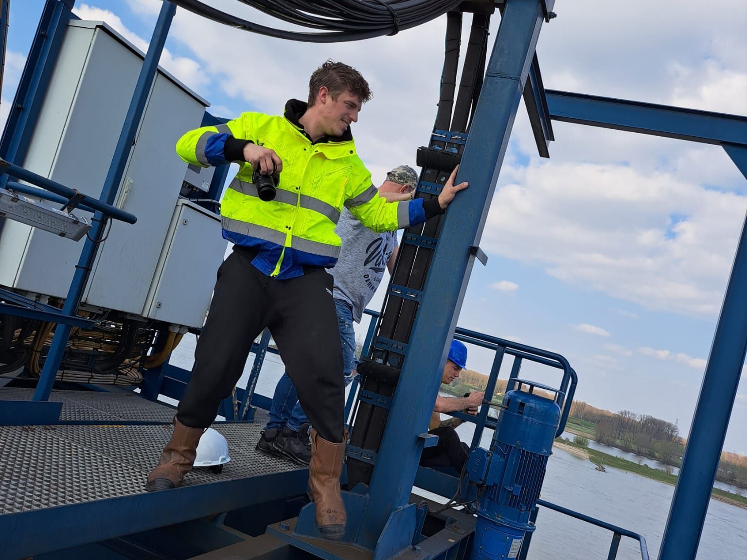Een man in een geel jasje staat bovenop een blauw bouwwerk.