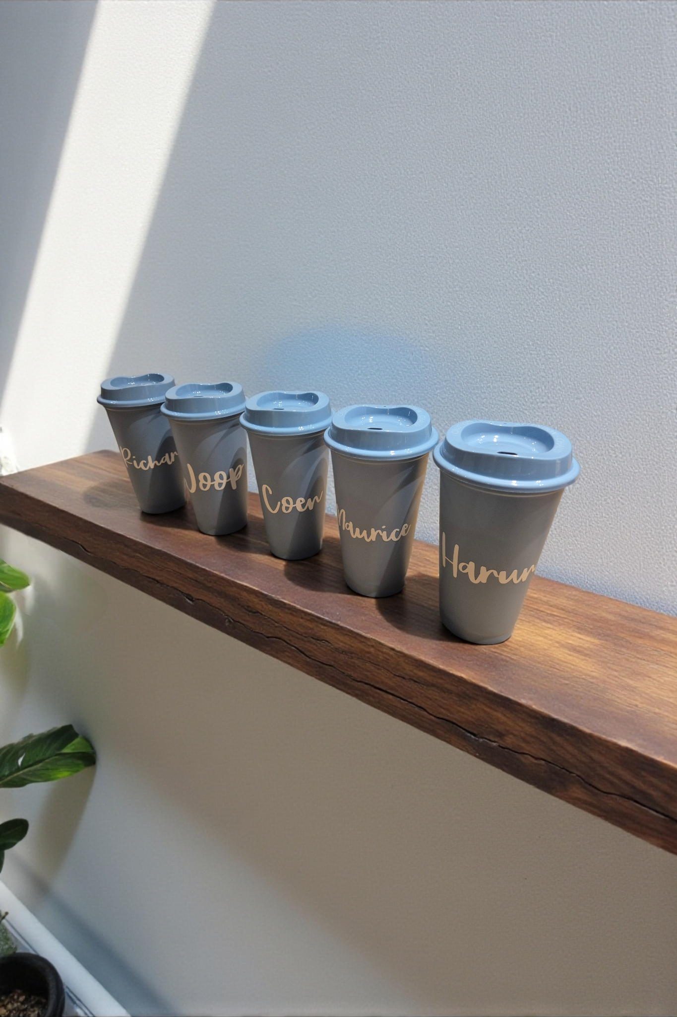 Vijf blauwe reisbekers met deksels en witte opdruk op een houten plank.